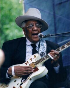 On Memorial Day 2013 it is fitting that I commemorate the legacy of three Earwig recording artists who served in the U.S. Military. There may be others on Earwig who did serve, though I am not aware of them. Homesick James Williamson, whose real name was William Henderson, was born in April 1910. He served in World War II in the Army and sustained a leg injury, which caused him to limp slightly, as one leg ended up shorter than the other. Homesick, as he came to be called by musicians and friends, perpetuated a mysterious image, rarely discussing details of his early life. He had a slightly Caribbean lilt to his accent, and often spoke in an almost mumbling manner which made it hard to understand him. He sometimes broke into fractured Spanish. He periodically moved, without much prior notice to anyone. During the 23 odd years that I knew him, he moved numerous times around Chicago, then to Nashville, Atlanta, Georgia, on to northern California, then to Covington, Tennessee and finally to Springfield, Missouri. Consequently another of his nicknames was Lookquick. Just as Honeyboy Edwards used to say “The world don’t owe me nothing,” Homesick used to tell folks “Look quick, ‘cause tomorrow I may be gone.” In fact, I took him to renew his passport in Chicago around the time of his Earwig recording session, and while I was waiting in my car several hours for him to come back from the passport office, he decided without telling me, to take off and take a cab back to his apartment over Rosa’s Lounge. He later told me that he was aggravated with Mama Rosa, his wife, who had decided to ride in the car with us because she wanted to spend some time with him. They had separated several years before and Homesick had moved out of town. During the time he was in Chicago for the recording session, he was staying with her. That was typical of Homesick, to make a seemingly spontaneous decision based on his feelings at the moment, without regard to the decision’s impact on those around him. Homesick was a proud man, who in most instances stood by his word. He also took pride in his ability to build as well as repair guitars, and in his musical knowledge. He was an outstanding guitarist, whose style was an amalgam of Tennessee and Mississippi Delta blues and Chicago 50’s electric blues. He was a contemporary of Memphis Minnie, John Lee “Sonny Boy” Williamson, Henry Townsend, Yank Rachel, Sleepy John Estes, Lonnie Johnson, Big Bill Broonzy, Sunnyland Slim, Elmore James and others. Homesick never quite got as much recognition as those great musicians. He is best known for playing with Elmore James, his cousin and his best known recordings are similar in style to Elmore’s. On his best days, he certainly could play as well as any of them. Playing with Homesick James was a challenge, because he tended to jump time, meaning that he made turnarounds somewhat unpredictably, so band members had to be able to anticipate what he might do. In that respect his playing was like Honeyboy Edwards’ style, though the two of them were unpredictable in different ways. I had the opportunity to produce one album of Homesick’s music, which I titled Goin’ Back In the Times, a phrase he used to introduce one of the songs on the recording. That album was supposed to be half a band album and half a solo album. He and I had agreed to hire some of the best Chicago musicians, who knew him and his style, to play on the session. So Homesick and I agreed on Sunnyland Slim – Albert Luandrew – on piano, Bob Stroger on bass, Robert Covington on drums, Lester Davenport on harmonica. Both Stroger and Covington were in Sunnyland’s band at that time. Lester had played with lots of folks, and had gotten his early tutelage from Homesick in the 1950s. The day before the session, we had a rehearsal scheduled at my house, and Homesick refused to come to it, though I had put him up at a motel close to my house. When I went to pick him up, the musicians were already at my house. He gave me no explanation, he just would not rehearse. The next day, August 27th 1992, in the studio at Delmark, Homesick early in the session, got into an argument with Bob, Robert, and Lester, claiming that they had been playing his music wrong. Homesick started cursing at these guys, and Stroger and Covington, though they knew Homesick was mercurial, verbally pushed back, saying that he was the one messing up, and that they were not going to take his verbal abuse. Lester, on the other hand, was more pragmatic, so he tried to cool things down so that we could finish the session. I expect that Sunnyland did the same as Lester, though I have no recollection of his reaction to Homesick’s obnoxiousness that day. I was freaking out, because I was spending a lot of money for the session and I was afraid of getting a bad session. In fact I did not use any of that session on the album and have not listened to it since. Back at the motel, Homesick acted as if nothing was wrong, though I was both very angry and hurt. Homesick just sat on his bed, playing Lonnie Johnson licks on his guitar as I vented. At that moment, when he was playing so beautifully, I felt as if he was intentionally messing with my mind, since in the studio he had not played like that. I extracted a commitment to him to play that type of material the next day, when we were scheduled to record solo and duo tracks, with Honeyboy Edwards as a guest on a few tracks. Fortunately for me and for my label’s body of work, on the second session, Homesick did what he said he would. He played some tunes he had not recorded before or since, with some beautiful licks covering his wide range of styles. He also waxed nostalgically on tape about his old friends Sunnyland Slim, Yank Rachel and Honeyboy Edwards, who played with him on a few tracks. Honeyboy had met Homesick in 1937 at the Tunica, Mississippi train station. What I ended up with was a beautiful traditional blues record, unlike most of the other recordings Homesick did in his lifetime. I love the record. One of these days, now that Protools software makes it so easy to edit and improve recordings, I will revisit the multitrack band recordings. Maybe I will discover something better than I remember from that very upsetting session with those blues masters when Homesick went off on them. My last memory of Homesick James is booking and watching Homesick on his last gig, the Maryport, England Blues Festival, the last weekend in July 2006. Homesick, Honeyboy Edwards with me on harmonica, and Robert Lockwood with his bassist Gene Schwartz, played that gig. Homesick was not feeling well, but like the trooper he was, played a 30 minute solo set, looking his usual dapper self in his suit, shined leather boots, and hat to match. He had stayed in bed most of the time over there, except to play his set and do a video interview with a documentary filmmaker. By the time we were ready to come back home, his feet had swollen such that he could not wear his boots. I offered him my purple Crocs so he would be more comfortable traveling. He wore those Crocs home, and got progressively sick that fall. He died at the age of 96 in a hospital in Springfield, Missouri December 13, 2006. His funeral was held in Covington, Tennessee, where his sister lived. He was preceded in death earlier that year, by his friends Henry Townsend on October 2, 2006 , Snooky Pryor on November 10, 2006, and Robert Lockwood on November 30, 2006. Check out these videos of Homesick James Homesick James plays the Blues Yank Rachell and Homesick James at Chicago Blues Fest 1993 Topic: Faces and Places